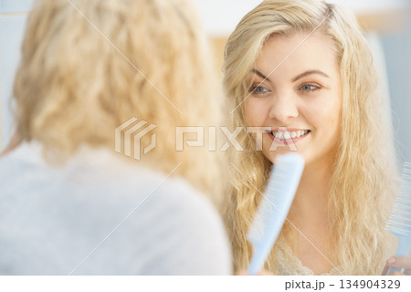 Woman getting ready in bathroom, combing hair. 134904329
