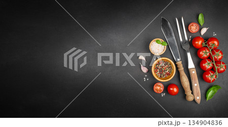 Cooking background with fresh cherry tomatoes, spices, cutlery and herbs on black slate surface with copy space 134904836