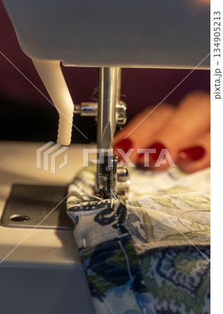 sewing machine needle in foreground with woman's hands out of focus in background sewing machine needle in foreground with woman's hands out of focus in background 134905213