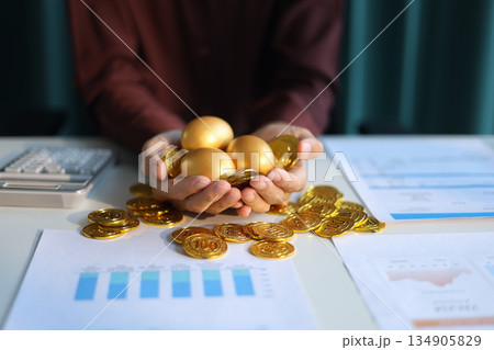 Gold coins and golden eggs in businessman's hands symbolizing financial growth and investment concepts. 134905829
