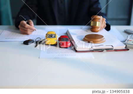 A man working on desk with gavel, contracts, and toy cars. Concept for Car Auction Legalities or Vehicle Bidding and Contracts. 134905838