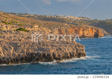 stunning cretan coastal landscape with sheer rocky cliffs meeting blue sea and houses on the hill 134906526