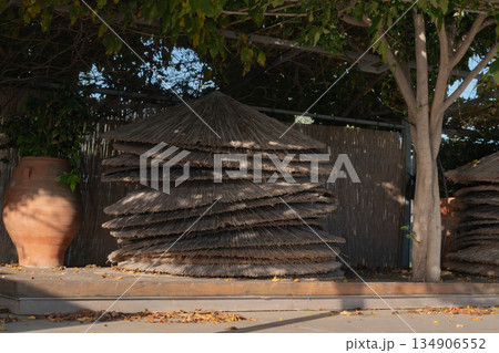 stack of woven straw beach umbrella roofs piled up after summer season closing on tropical resort 134906552