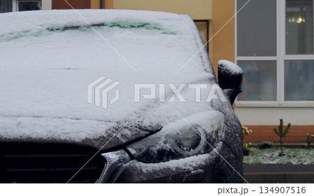Headlight of gray car parked in front of residential building covered with snow and ice 134907516