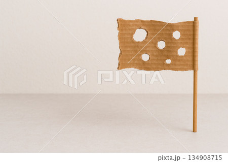 Cardboard flag with holes on a light background. Space for text. Cardboard flag with holes on a light background. Space for text. 134908715