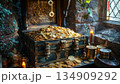 A treasure chest of gold coins rests on a table by a window 134909292