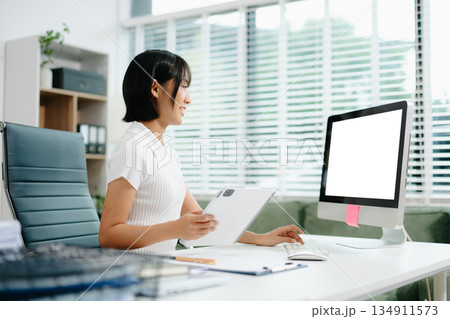 Confident Asian woman with a smile standing holding notepad and tablet at the modern office. Confident Asian woman with a smile standing holding notepad and tablet at the modern office. 134911573