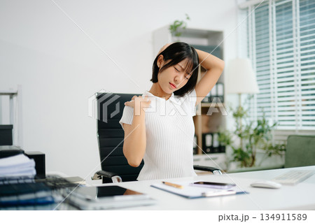 A young office woman suffering from neck and back pain while working at her desk, showing workplace stress, poor posture, and the need A young office woman suffering from neck and back pain while working at her desk, showing workplace stress, poor posture, and the need 134911589