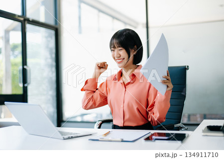 Asian business woman are delighted and happy with the work they do on their tablet, laptop and taking notes at the office. 134911710