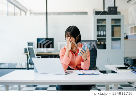Asian business woman is stressed, bored, and overthinking from working on a tablet at the modern office. Asian business woman is stressed, bored, and overthinking from working on a tablet at the modern office. 134911716