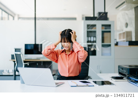 Stressed Asian Businesswoman Feeling Overworked at office desk with laptop. 134911721