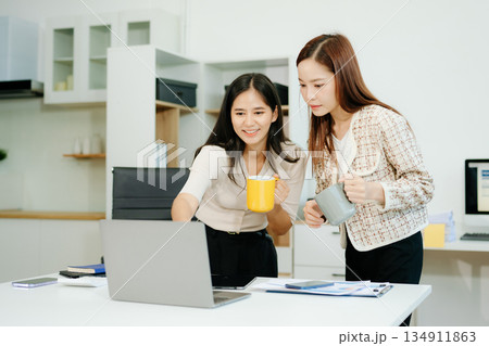 Asian businesswomen enjoying coffee and teamwork at office desk while working on laptop. Great for themes of success, collaboration Asian businesswomen enjoying coffee and teamwork at office desk while working on laptop. Great for themes of success, collaboration 134911863
