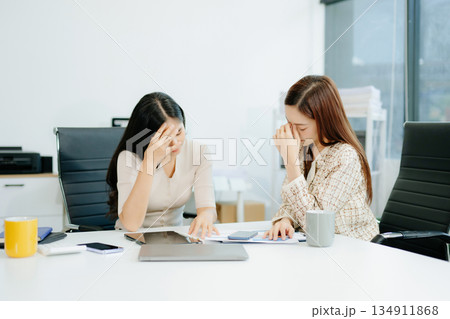 Asian woman comforts her distressed coworker in office. Concept of workplace stress, burnout, empathy, and emotional support in professional environments. Asian woman comforts her distressed coworker in office. Concept of workplace stress, burnout, empathy, and emotional support in professional environments. 134911868