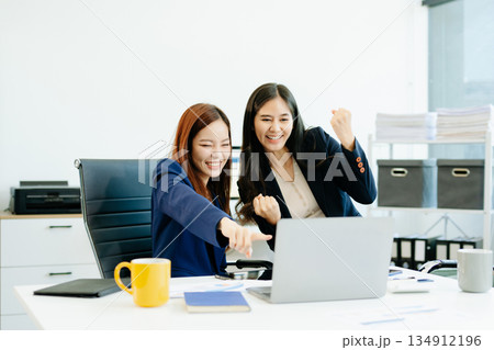 Two Asian businesswomen in suits analyze reports together at a modern office desk. A scene of teamwork, leadership Two Asian businesswomen in suits analyze reports together at a modern office desk. A scene of teamwork, leadership 134912196
