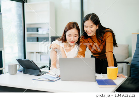 Businesswomen work and discuss their business plans. A woman employee explains and shows her colleague Businesswomen work and discuss their business plans. A woman employee explains and shows her colleague 134912212