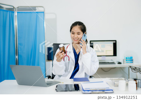 Confident young  female doctor in white medical uniform sit at desk working on computer. 134912251