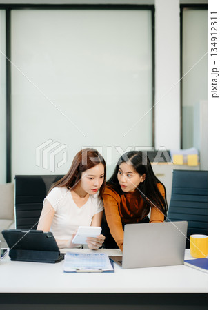 Businesswomen work and discuss their business plans. A woman employee explains and shows her colleague Businesswomen work and discuss their business plans. A woman employee explains and shows her colleague 134912311