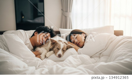 朝の光の中で犬と添い寝する若いカップルの穏やかな寝顔 134912365