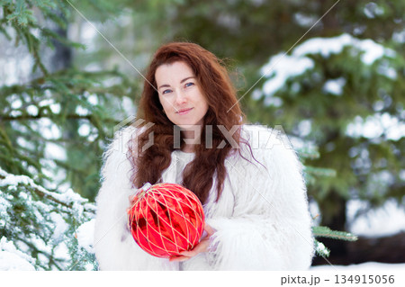 Woman in a fur coat holding a Christmas ball in the forest. Woman in a fur coat holding a Christmas ball in the forest. 134915056