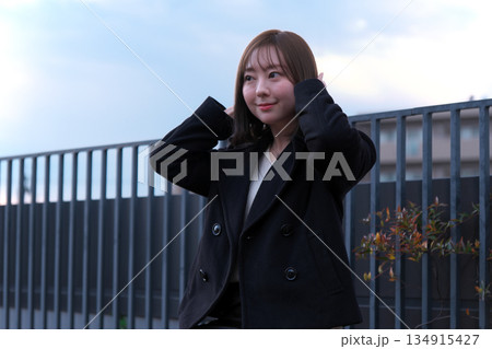 屋外で風に吹かれながら髪を直す黒いコートの女性・冬の夕暮れのポートレート 屋外で風に吹かれながら髪を直す黒いコートの女性・冬の夕暮れのポートレート 134915427