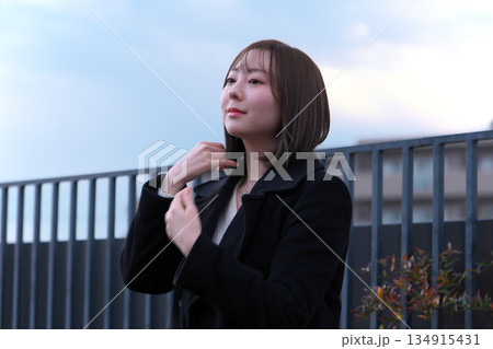 屋外で風に吹かれながら髪を直す黒いコートの女性・冬の夕暮れのポートレート 屋外で風に吹かれながら髪を直す黒いコートの女性・冬の夕暮れのポートレート 134915431