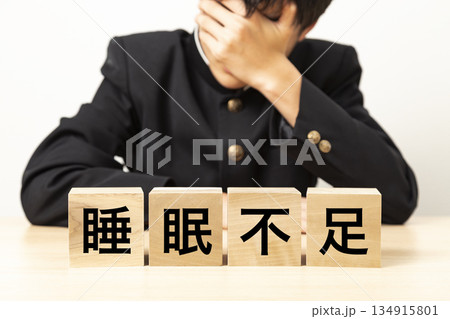 「睡眠不足」と書かれたブロックと悩む男子学生 134915801