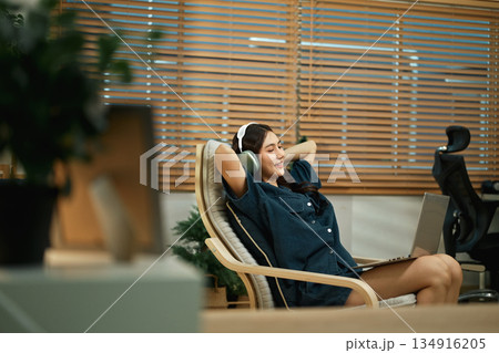Smiling woman wearing headphones listen to music playing in laptop computer 134916205