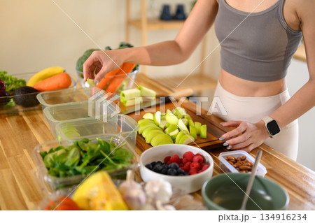Closeup of a woman hand placing freshly cut fruits and vegetables into food storage containers, meal prep, and food preservation 134916234