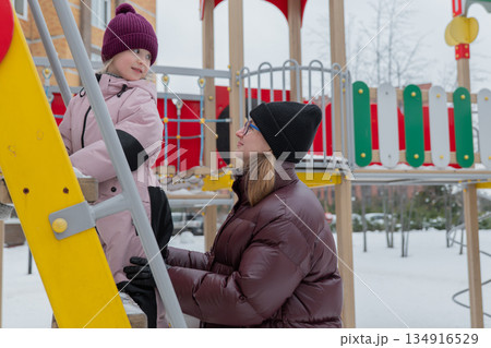 Girl with rosy cheeks on colorful structure, Child with cheerful expression on winter playground structure, Adventurous girl with knit hat and rosy cheeks on snowcovered play equipment Girl with rosy cheeks on colorful structure, Child with cheerful expression on winter playground structure, Adventurous girl with knit hat and rosy cheeks on snowcovered play equipment 134916529