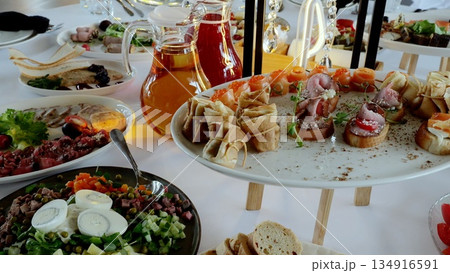 Elegant catering spread featuring gourmet appetizers, colorful salads, crisp bruschetta, and refreshing drinks artfully displayed on white draped table surface Elegant catering spread featuring gourmet appetizers, colorful salads, crisp bruschetta, and refreshing drinks artfully displayed on white draped table surface 134916591