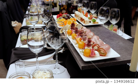 Wine glasses surrounding gourmet appetizers resting on dramatic black white checkered tablecloth, highlighting elegant catered dining experience Wine glasses surrounding gourmet appetizers resting on dramatic black white checkered tablecloth, highlighting elegant catered dining experience 134916612