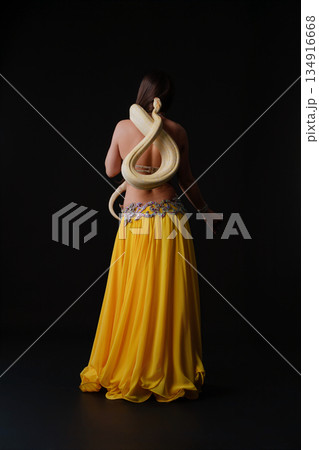 Woman dances with a snake during a performance on a dark stage Woman dances with a snake during a performance on a dark stage 134916668