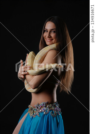 Woman performs dance while holding a snake in a dark setting during an evening event 134916671