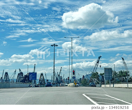 Construction cranes and vehicles on a busy road under a cloudy blue sky 134919258