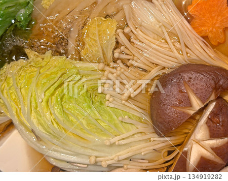 Close-up view of a bubbling hot pot with napa cabbage, enoki mushrooms, and shiitake 134919282