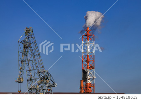white smoke from smokestack and big crane of a steel factory with blue sky 134919615