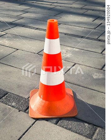 Orange traffic cone on an urban paved pathway in sunlight. 134920084