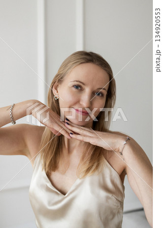 Smiling elegant woman in silk top posing indoors with hands under chin Smiling elegant woman in silk top posing indoors with hands under chin 134920553