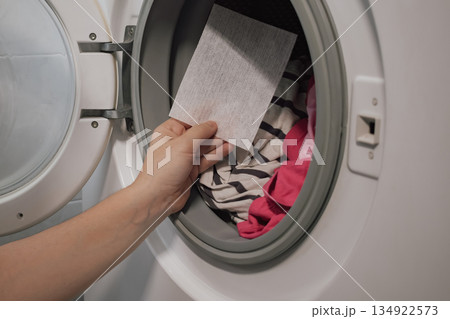 woman's hand placing color catcher sheet into washing machine for mixed colored laundry woman's hand placing color catcher sheet into washing machine for mixed colored laundry 134922573