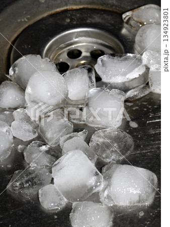 Melting ice cubes dripping down a sink plug drain silver metal basin Melting ice cubes dripping down a sink plug drain silver metal basin 134923801