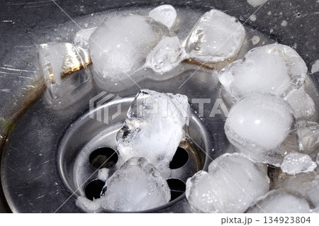 Melting ice cubes dripping down a sink plug drain silver metal basin Melting ice cubes dripping down a sink plug drain silver metal basin 134923804