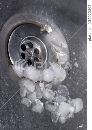 Melting ice cubes dripping down a sink plug drain silver metal basin Melting ice cubes dripping down a sink plug drain silver metal basin 134923807