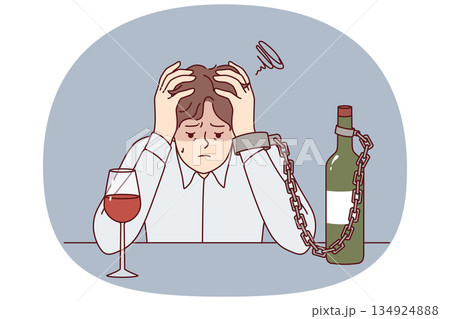 Man suffering from alcohol addiction is chained to bottle of wine, sitting at table clutching head Man suffering from alcohol addiction is chained to bottle of wine, sitting at table clutching head 134924888