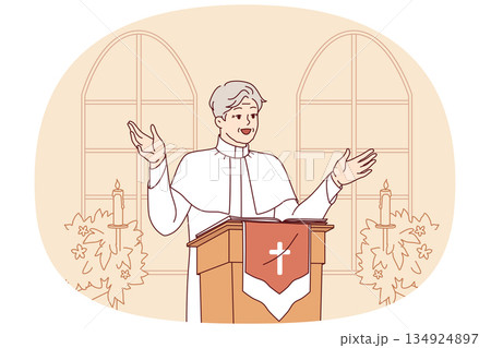 Man priest with smile leads sermon in catholic church, standing behind podium with crucifix Man priest with smile leads sermon in catholic church, standing behind podium with crucifix 134924897