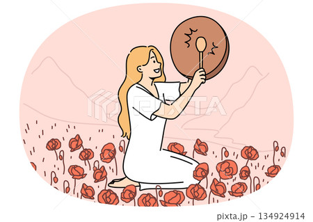 Woman shaman with drum sits in poppy field and plays ethnic musical instrument to bring about rain 134924914
