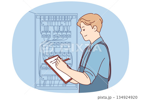 Man inspector checks electrical equipment installed in metal power panel, makes notes in clipboard 134924920