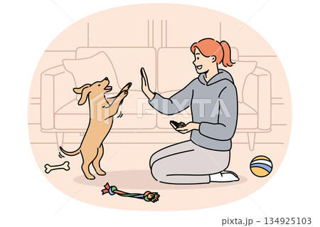 Woman trains dog while sitting on floor near sofa and giving food to puppy after following command 134925103