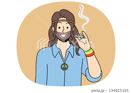 Hippie man smoking cannabis and smiles, standing with symbol of pacifist subculture on chest 134925105