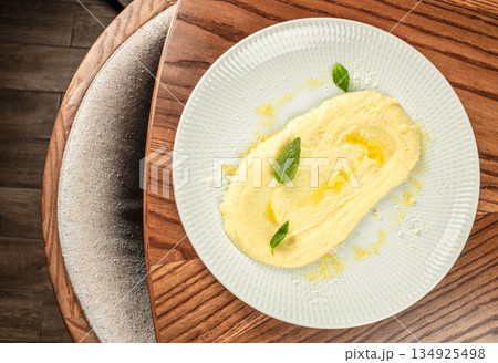 Creamy mashed potatoes with butter olive oil and basil served on plate on wooden table, top view, copy space 134925498