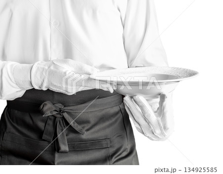 Professional waiter in white uniform holding empty plate isolated on white background, restaurant service and hospitality concept 134925585
